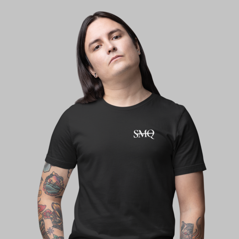 A person facing the camera wears a black t-shirt with the white 'SMQ' logo on the chest; their long, straight hair and tattooed arms are visible.