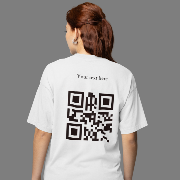 A person with brown hair in a ponytail is wearing a white t-shirt with the back visible, showing the words "Your text here" printed above a black QR code.