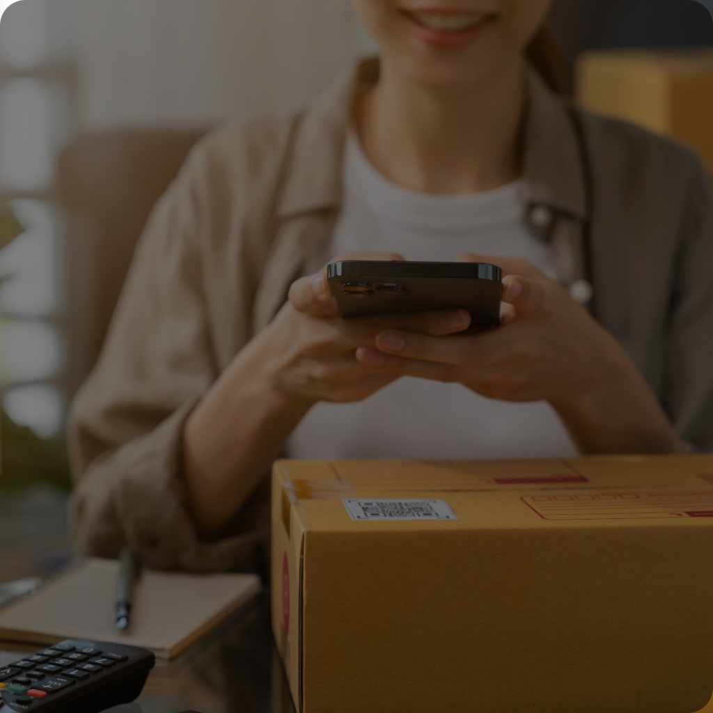 A delivery person smiles while holding a smartphone that scans a QR code on a package, indicating the use of QR codes for logistics and package tracking.