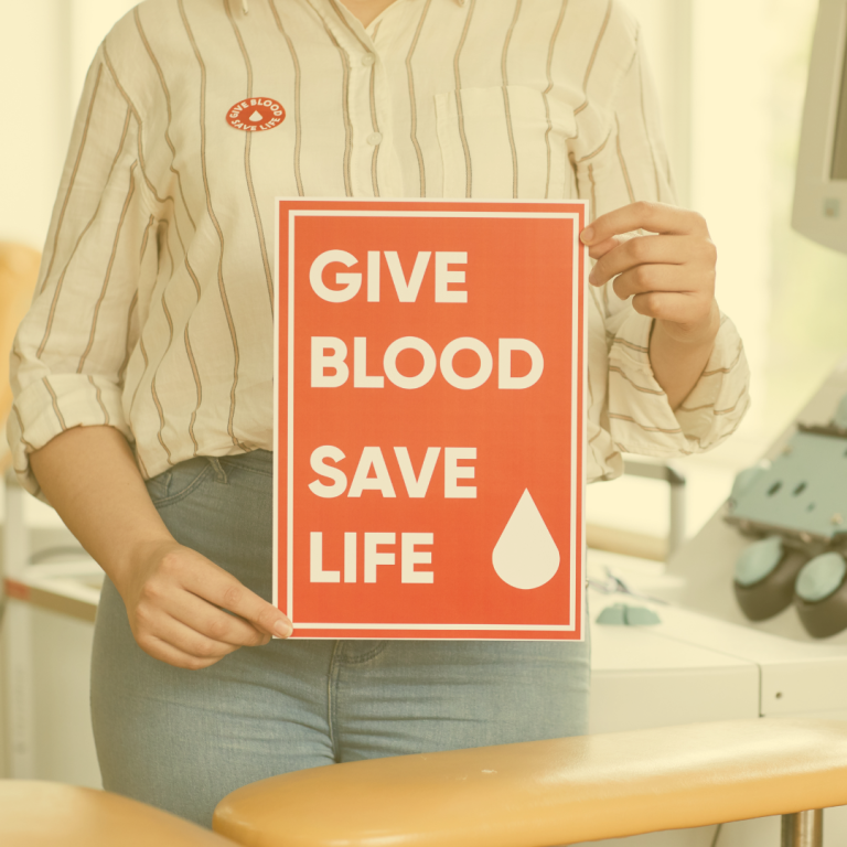 A person holding a 'Give Blood Save Life' sign inside a medical facility, promoting the critical message of blood donation.